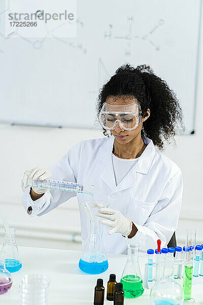 Forscherin mit Schutzbrille gießt bei der Arbeit im Labor eine Flüssigkeit ein