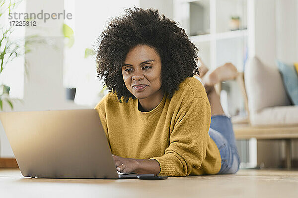 Lächelnde Frau  die einen Laptop benutzt  während sie zu Hause liegt