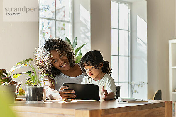 Lächelnde Mutter und Tochter schauen auf ein digitales Tablet  während sie im Wohnzimmer sitzen