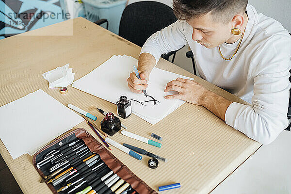 Hipster junger Mann übt Kalligraphie auf Papier im Atelier