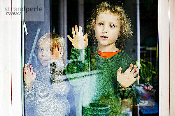 Junge mit Schwester schaut durch Glastür nach draußen
