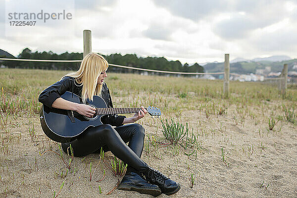 Junge Frau spielt Gitarre  während sie auf Sand sitzt