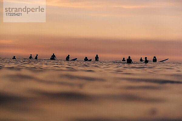 Touristen mit Surfbrettern im Meer während der Ferien bei Sonnenuntergang