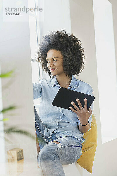 Junge Frau mit digitalem Tablet am Fenster sitzend