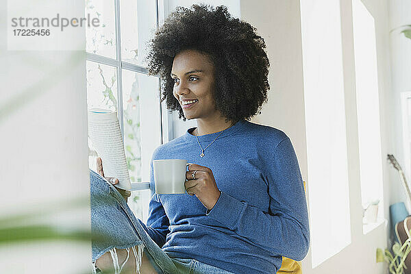 Frau mit Kaffeetasse und Buch am Fenster zu Hause
