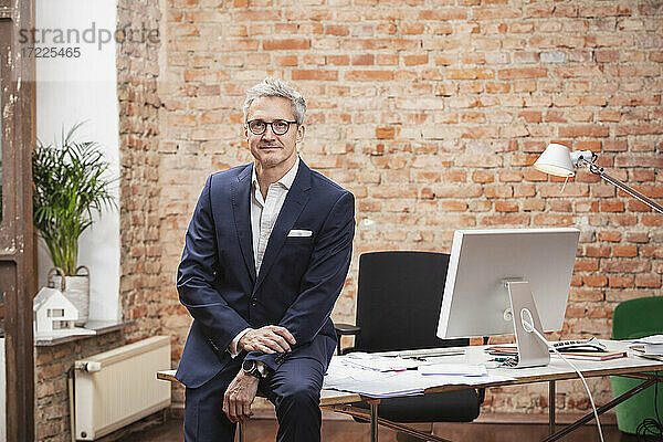 Reifer Geschäftsmann mit Brille sitzt am Schreibtisch bei der Arbeit