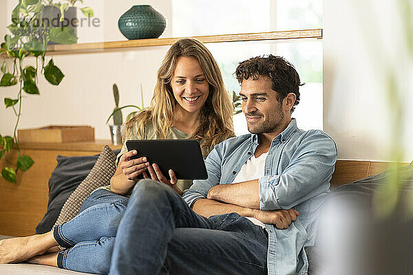 Lächelnde Frau mit Freund  die zu Hause auf ein digitales Tablet schaut