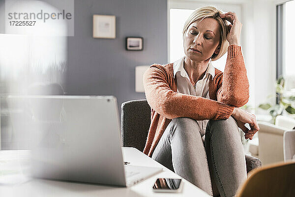 Reife müde Geschäftsfrau mit geschlossenen Augen sitzt im Büro zu Hause