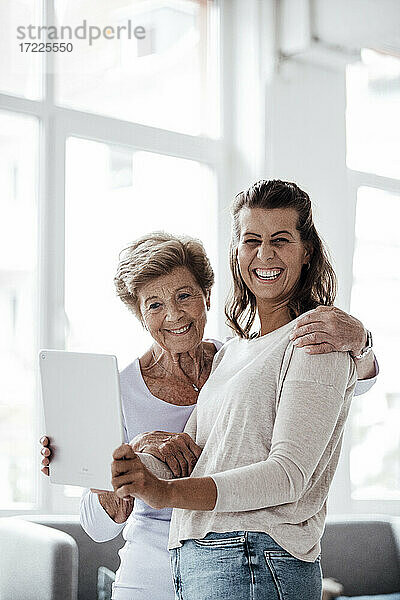 Fröhliche junge Frau hält digitales Tablet bei ihrer Großmutter zu Hause