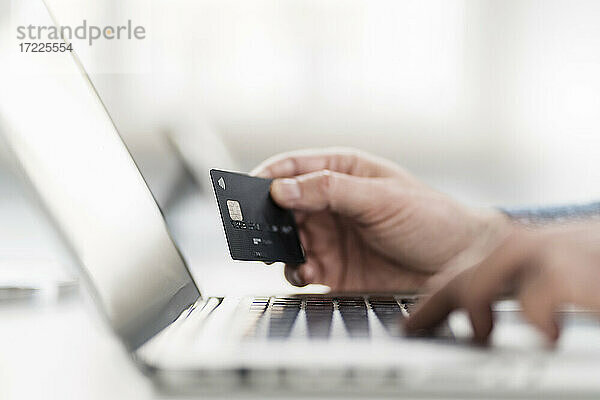 Hand eines Geschäftsmannes  der einen Laptop benutzt und eine Kreditkarte am Arbeitsplatz hält