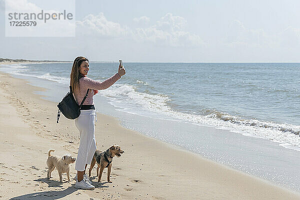 Frau mit Hunden spricht Selfie durch Smartphone am Strand während sonnigen Tag