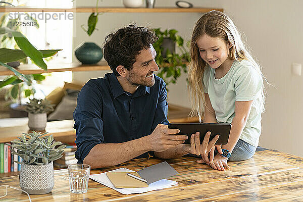 Glücklicher Vater mit digitalem Tablet  der seine Tochter beim Diskutieren zu Hause ansieht