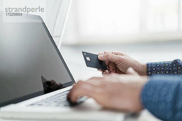 Hand eines männlichen Unternehmers  der einen Laptop benutzt und eine Kreditkarte im Büro hält