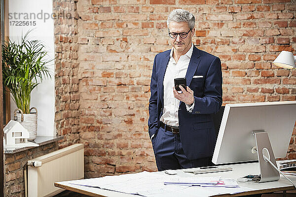 Männlicher Architekt  der ein Smartphone benutzt  während er am Schreibtisch im Büro steht