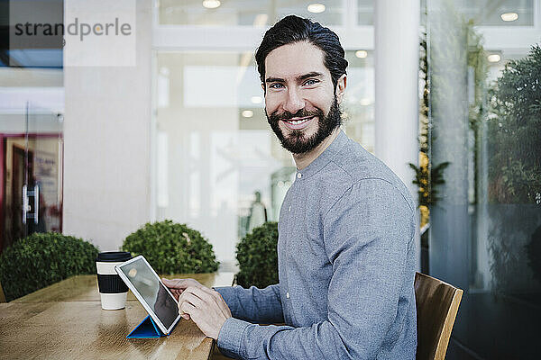 Lächelnder Geschäftsmann mit digitalem Tablet auf dem Schreibtisch am Arbeitsplatz