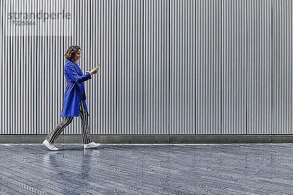 Berufstätige Frau benutzt Smartphone beim Gehen auf dem Fußweg