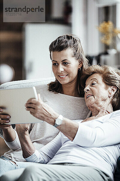 Ältere Frau verwendet digitales Tablet  während sie sich bei ihrer Enkelin zu Hause entspannt