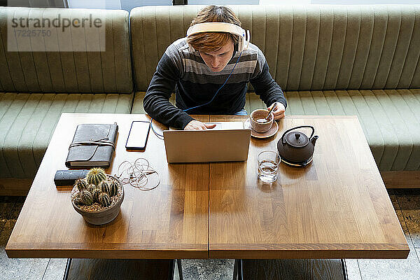 Geschäftsmann  der einen Laptop mit einer Teetasse benutzt  während er am Schreibtisch im Büro sitzt