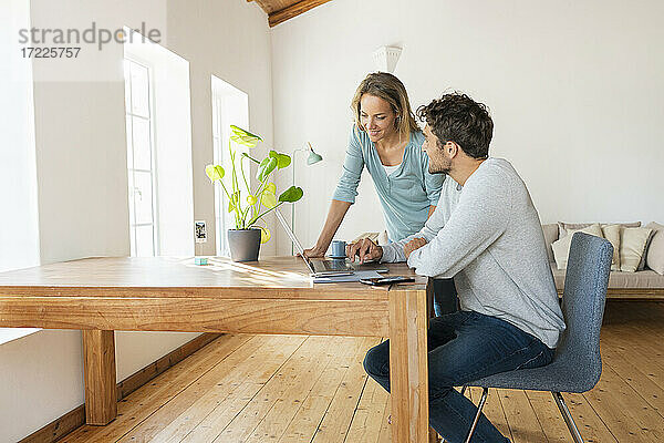 Mann diskutiert mit Freundin bei der Arbeit am Laptop im Home Office