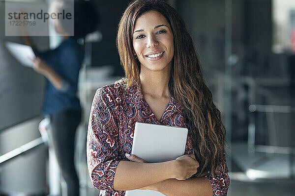 Lächelnde Geschäftsfrau mit digitalem Tablet im Büro stehend