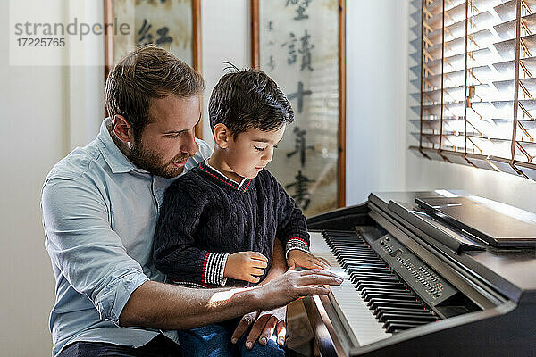 Junge lernt zu Hause auf dem Schoß des Vaters Klavier