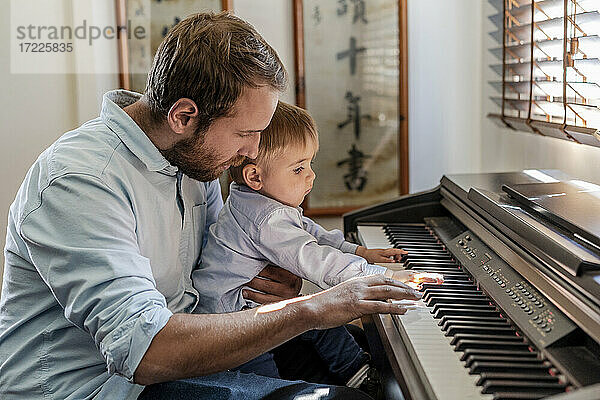 Vater gibt seinem Sohn Klavierunterricht  der zu Hause auf dem Schoß sitzt