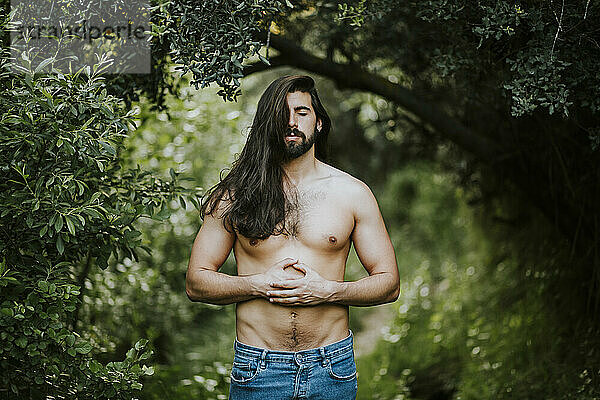 Mann ohne Hemd mit geschlossenen Augen steht und entspannt sich im Wald