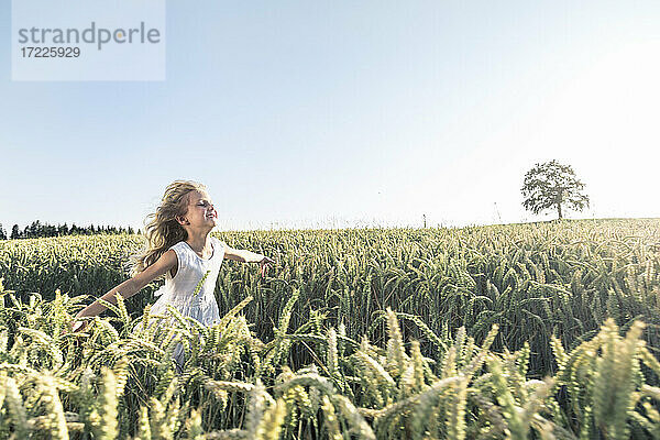 Lächelndes Mädchen mit ausgestreckten Armen läuft auf einem Feld