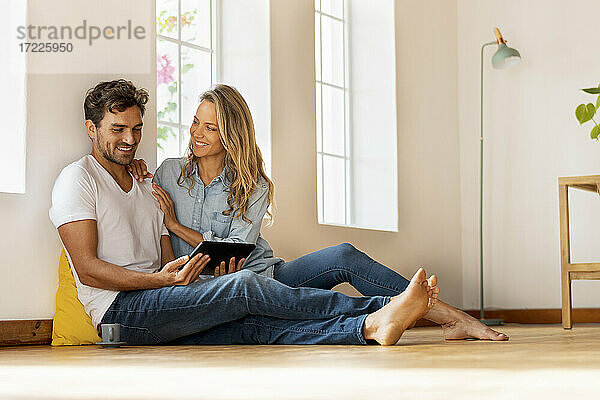 Schöne Frau sieht ihren Freund an  der ein digitales Tablet benutzt  während er zu Hause auf dem Boden sitzt