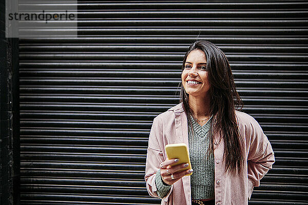 Lächelnde Frau schaut weg  während sie vor einem geschlossenen Fensterladen steht