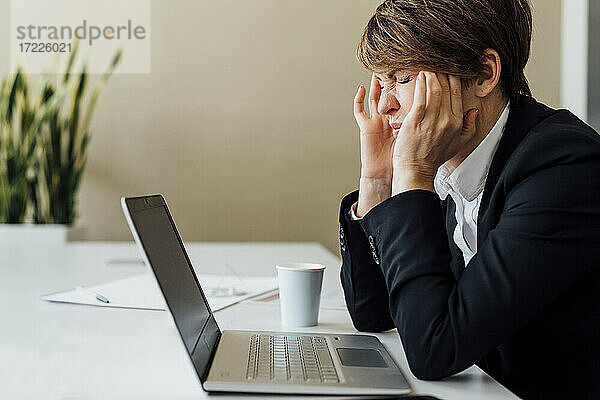 Frustrierte Geschäftsfrau  die vor einem Laptop am Schreibtisch sitzt