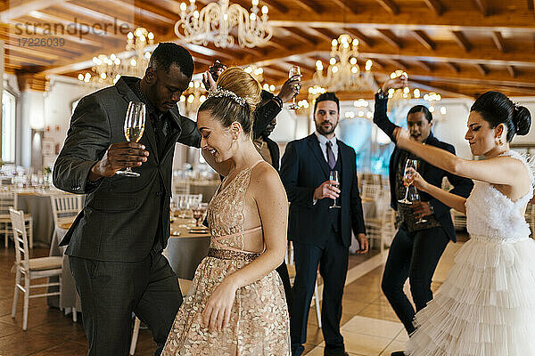 Männliche und weibliche Freunde tanzen bei einem Bankett und halten eine Champagnerflöte in der Hand