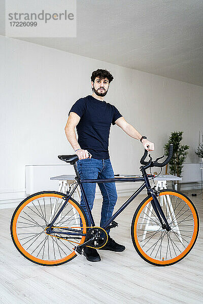 Junger Mann mit Fahrrad vor dem Haus stehend