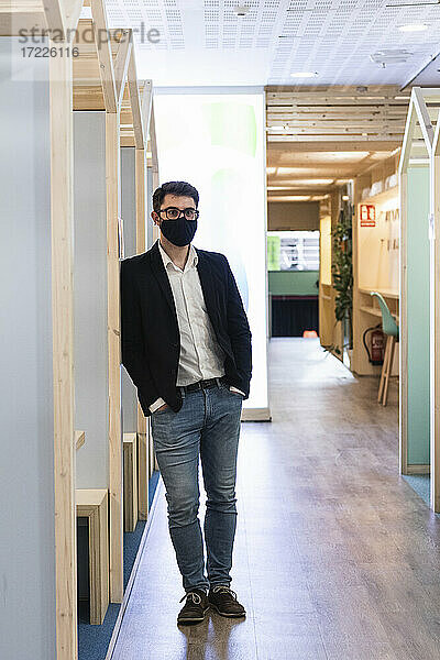 Junger Unternehmer mit Gesichtsmaske  der mit den Händen in den Taschen in einer Cafeteria steht