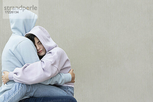 Mädchen umarmt  während sie auf dem Schoß ihres Freundes an der Wand sitzt