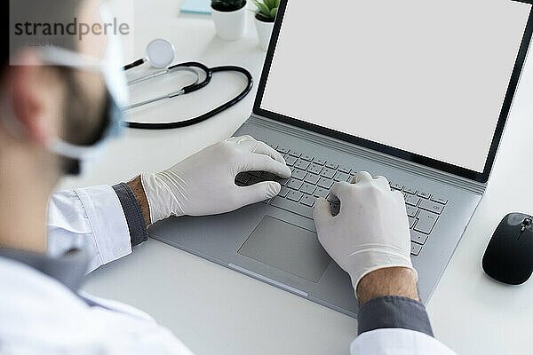 Männlicher Arzt mit Laptop im Krankenhaus während COVID-19