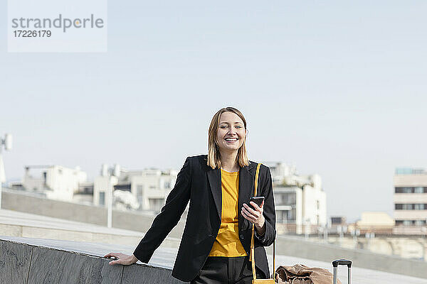 Lächelnde Unternehmerin stehend mit Mobiltelefon