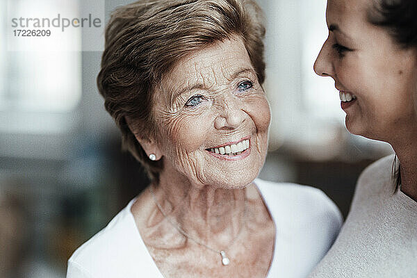 Glückliche ältere Frau  die von ihrer lächelnden Enkelin zu Hause weggeschaut wird
