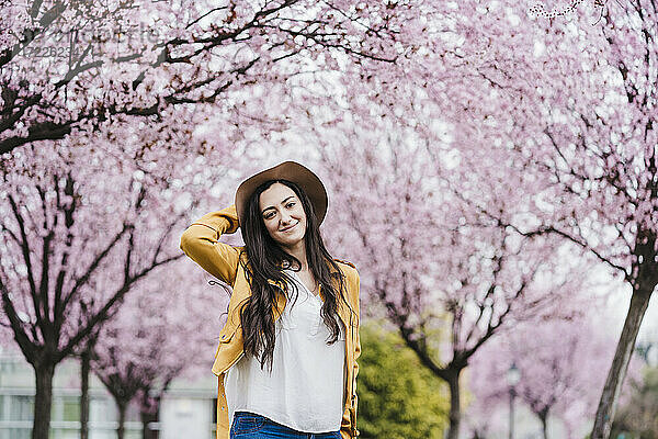 Lächelnde Frau mit Sonnenhut vor einem Frühlingsbaum stehend