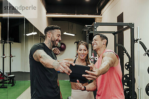 Fröhliche Freunde machen ein Selfie mit ihrem Smartphone im Fitnessstudio