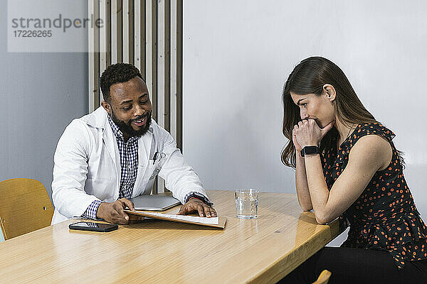 Männlicher Arzt berät junge Patientin am Schreibtisch in einer Klinik