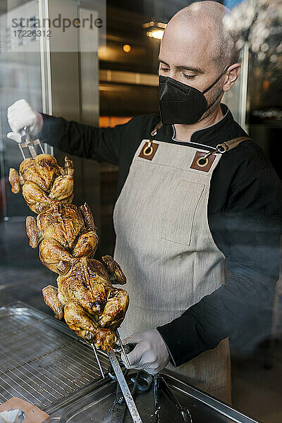 Männlicher Koch mit gegrilltem Tandoori-Huhn  gesehen durch Glas in der Küche während der Pandemie