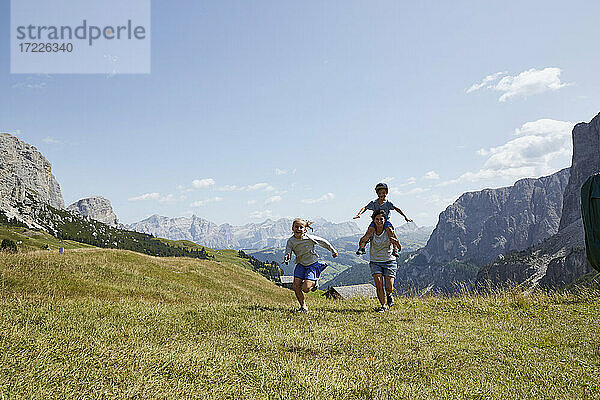 Frau trägt ihren Sohn auf den Schultern  während sie mit ihrer Tochter auf einem Berg läuft