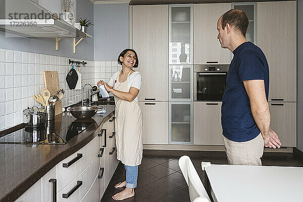 Lächelnde Frau im Gespräch mit ihrem Mann bei der Zubereitung von Speisen in der Küche zu Hause