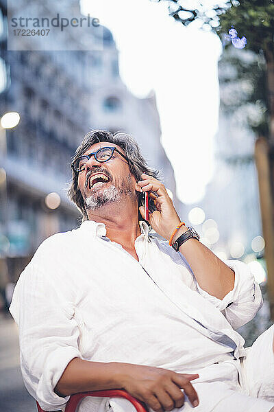 Älterer Mann lacht  während er in einem Straßencafé in Madrid mit seinem Handy telefoniert