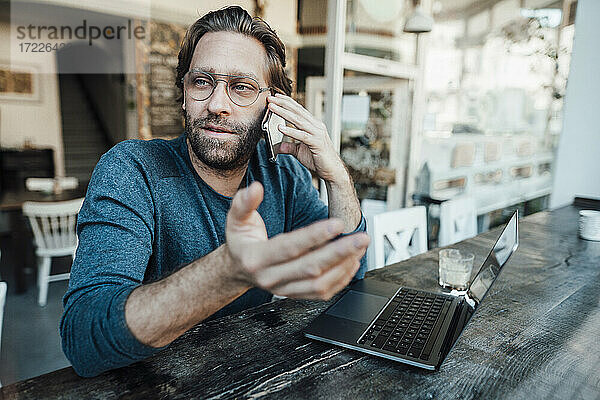 Männlicher Unternehmer  der in einem Café mit seinem Laptop telefoniert