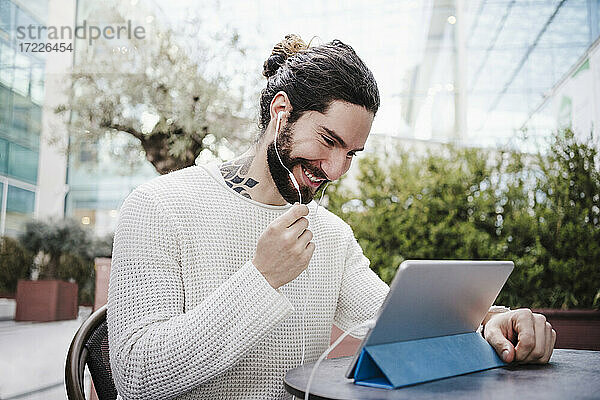 Lächelnder Mann  der einen Videoanruf über ein digitales Tablet in einem Straßencafé führt