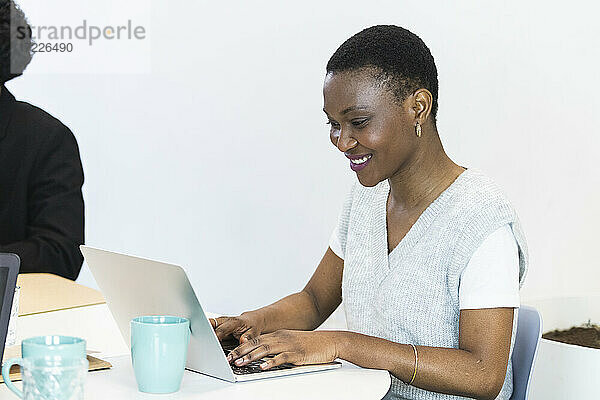 Lächelnder mittlerer erwachsener Unternehmer  der einen Laptop bei der Arbeit im Büro benutzt