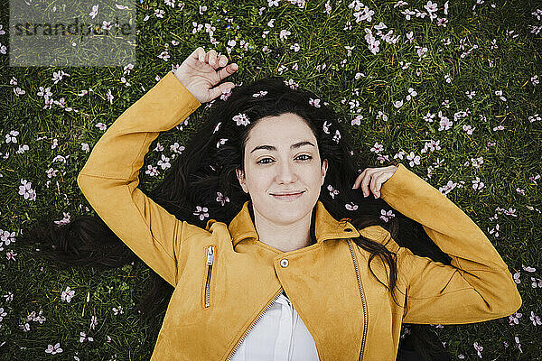 Lächelnde schöne Frau mit Blumen im Haar im Gras liegend