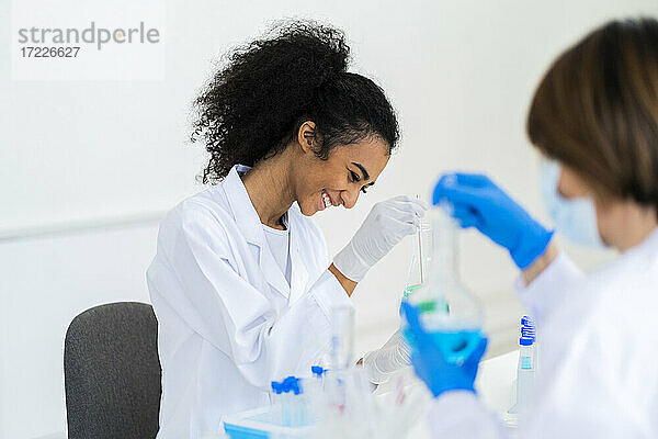 Lächelnde Forscherin bei der Arbeit mit einem Mitarbeiter während eines Experiments im Labor